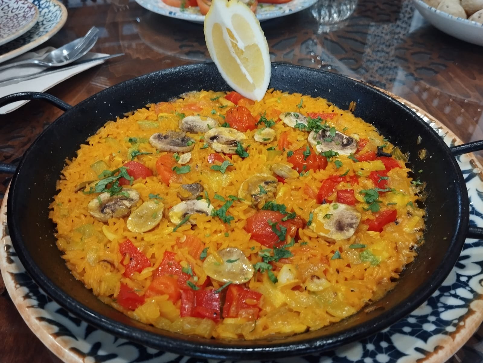 Paella with peppers and mushrooms in the pan, with a wedge of lemon
