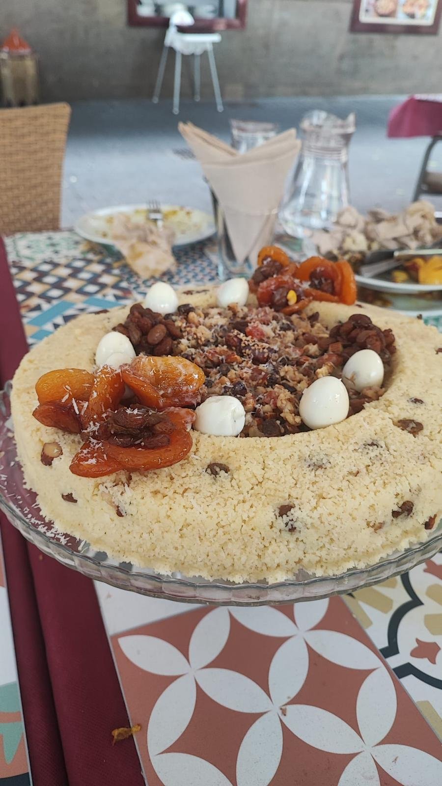 Sweet couscous topped with dried apricots, raisins and nuts on a glass stand
